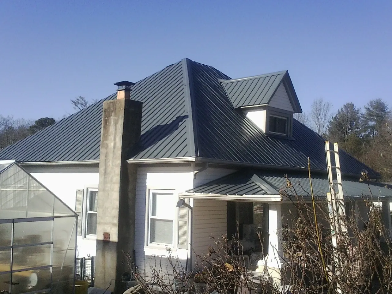 Dark blue standing seam metal roof on a white farmhouse with dormer — Slate & Tile Roof Repair by Roofing Brothers in Cumberland City