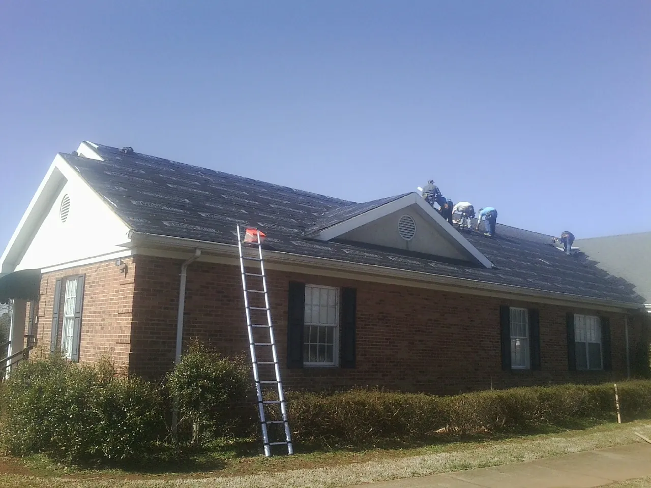 Crew tearing shingles off a brick ranch roof with a ladder set — Metal Roof Repair work by our crew in Cumberland City