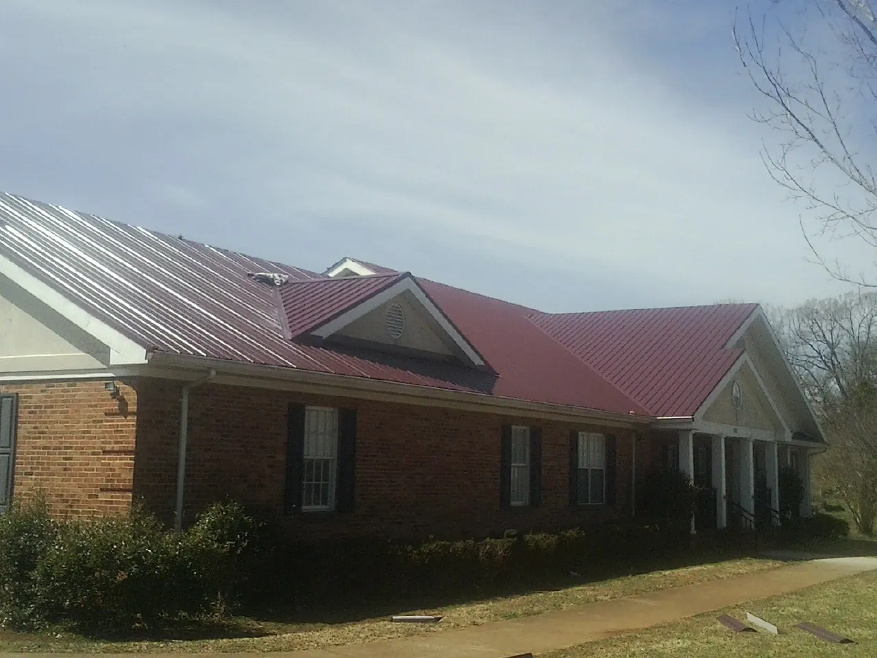 Red metal roof with gabled entries on a long brick building, from a Hail Damage Roof Repair job in Cumberland City