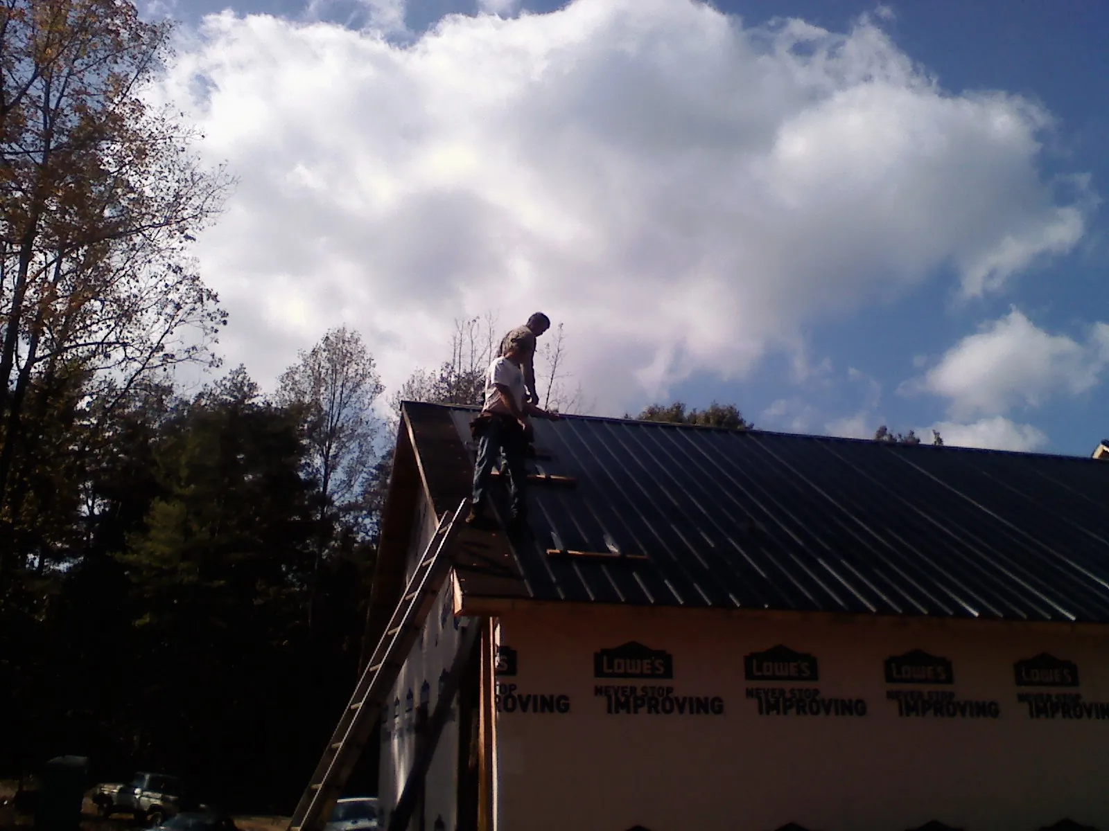 Roofer fastening dark metal panels high against a cloudy sky, from a Roof Inspection job in Cumberland City