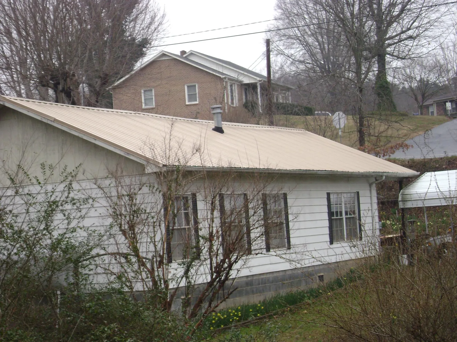 Tan metal roof on a white sided house set into a hillside — Commercial Roofing by Roofing Brothers in Cumberland City